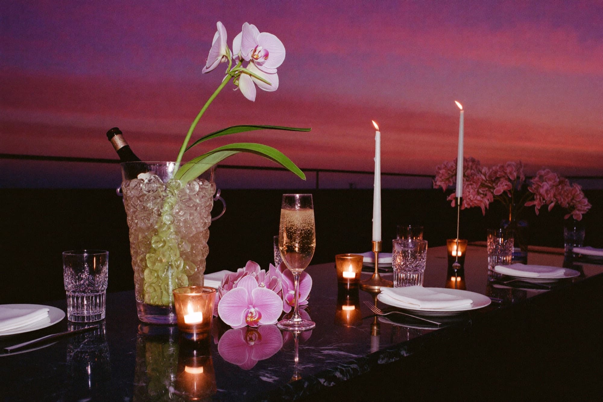 Tavolo apparecchiato su una terrazza al tramonto, orchidee e candele